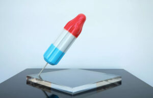 Sculptural artwork of a red, white, and blue Bomb Pop-style popsicle by Derrick Adams, angled on a clear acrylic base