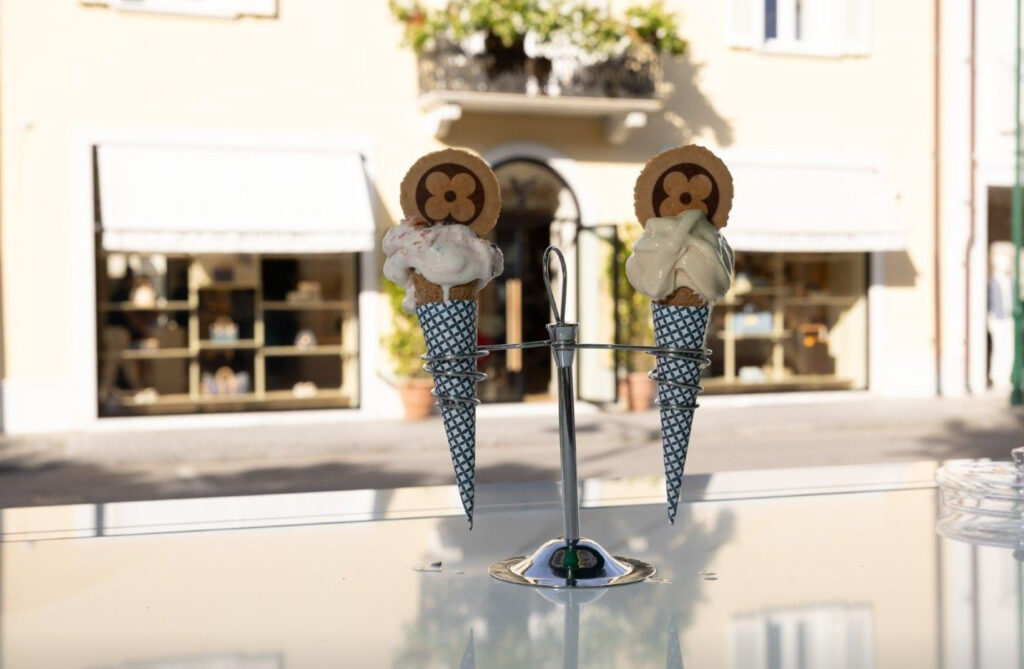 Branded ice cream cone from Louis Vuitton pop-up gelateria in Forte dei Marmi, held against blue sky with palm trees