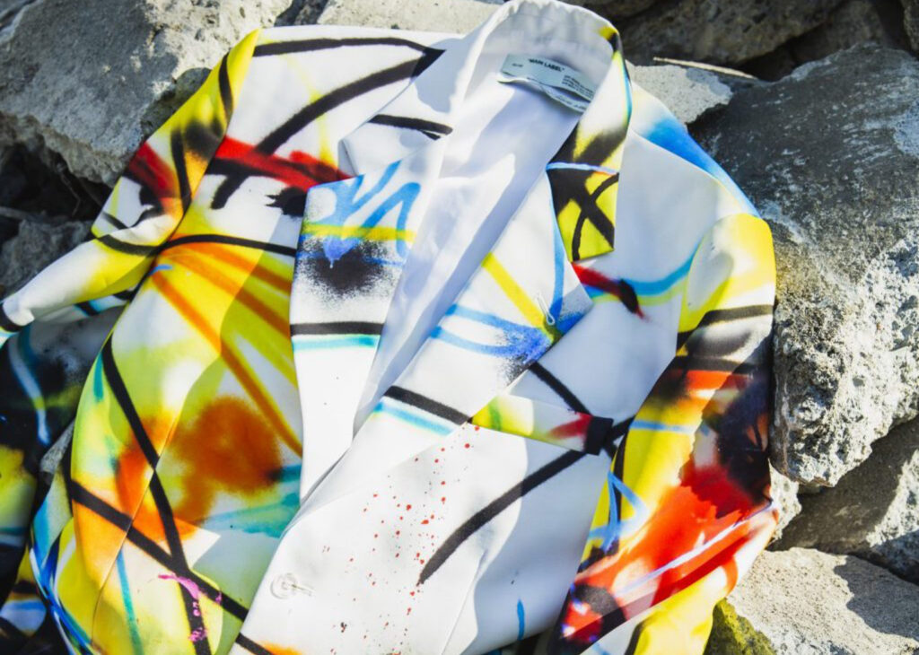 Graffiti-painted OFF-WHITE blazer by Virgil Abloh featuring vibrant spray art by Futura, draped over natural stone