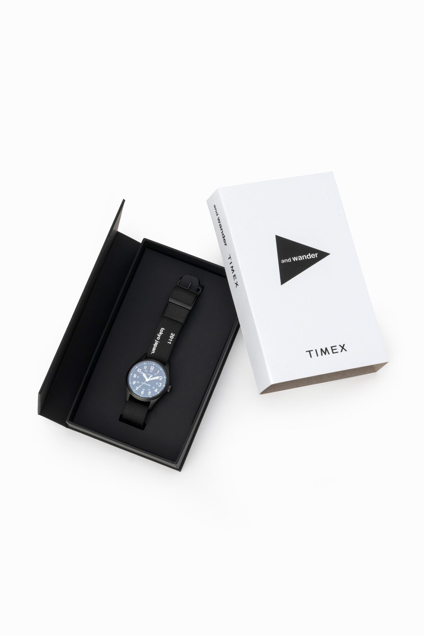 A sleek Timex × And Wander Expedition North Field Post Solar watch in matte titanium finish, featuring luminous numerals and a durable fabric strap with reflective stitching, set against a minimalist outdoor-inspired background