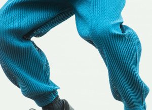 Close-up of blue HOMME PLISSÉ ISSEY MIYAKE mesh pants, highlighting the intricate pleated texture and perforated fabric design, shown in dynamic motion