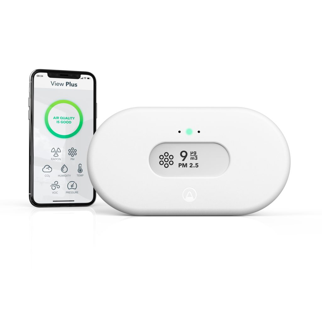Airthings View Plus indoor air quality monitor with e-ink display showing PM2.5, CO₂, and radon levels, placed in a modern home