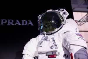 Close-up of the AxEMU lunar spacesuit co-designed by Prada and Axiom Space, displayed against a black background with Prada logo, featuring reflective helmet visor and technical suit details