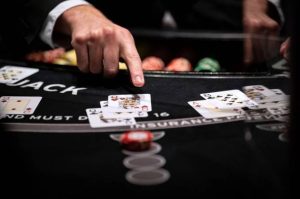 A close-up view of a blackjack table with a dealer's hand pointing at a pair of queens among multiple playing cards and colorful casino chips in the background