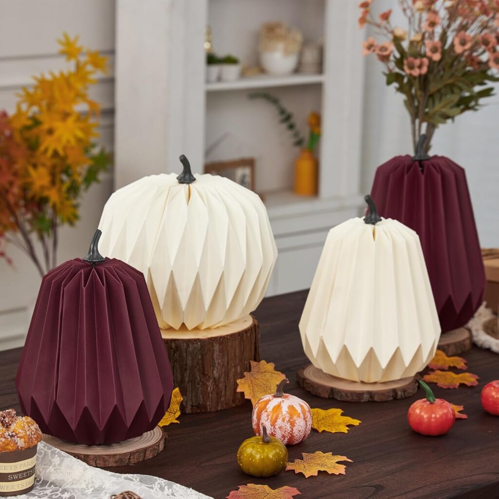 “Fall table decorated with 3D honeycomb paper pumpkins in white and burgundy, displayed on wooden bases with autumn leaves and small gourds.”