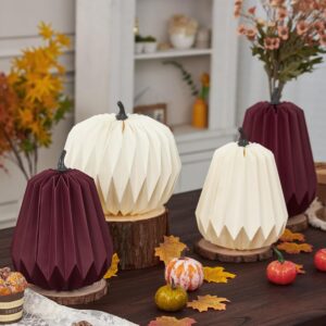 “Fall table decorated with 3D honeycomb paper pumpkins in white and burgundy, displayed on wooden bases with autumn leaves and small gourds.”