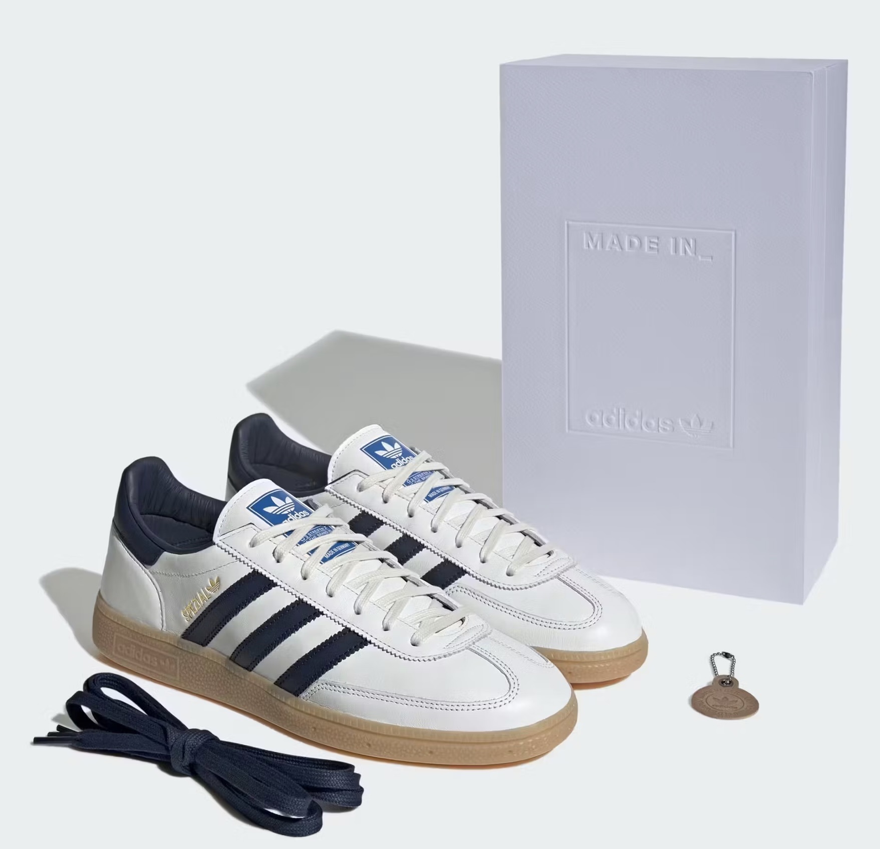 Adidas Spezial “Made in Germany” sneakers in white leather with navy stripes and gum sole, displayed with a premium white embossed box, extra navy laces, and a Trefoil keychain.