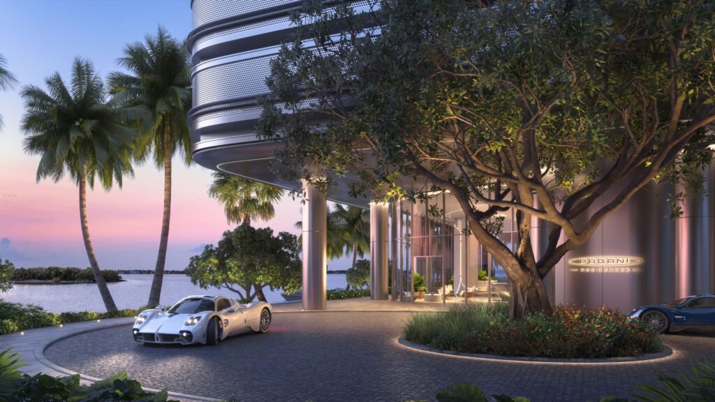 Exterior view of Pagani Residences in Miami, featuring a silver Pagani hypercar parked under palm trees at sunset, with the building’s perforated aluminum façade and illuminated Pagani logo visible.