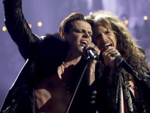 Yungblud and Steven Tyler singing passionately together on stage, sharing a microphone under dramatic concert lighting during their performance of “My Only Angel.
