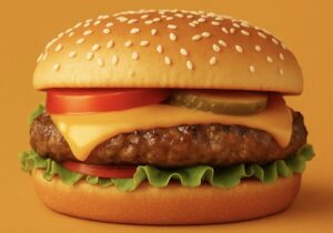 Close-up of a classic cheeseburger with a sesame seed bun, melted American cheese, lettuce, tomato, pickle slices, and a juicy beef patty on an orange background.
