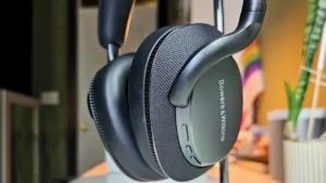 Close-up of Bowers & Wilkins Px7 S3 over-ear headphones in black, showing the textured earcup design, premium matte finish, and soft leather padding, photographed indoors with blurred background decor.