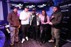 The Punchline Academy show. They stand together in front of screens displaying the Punchline Academy logo, with microphones and studio equipment visible in the room.