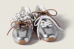 Pair of Miu Miu x New Balance 530 sneakers in metallic silver with mismatched laces, combining white, brown, and patterned details, from the Fall 2025 collection.