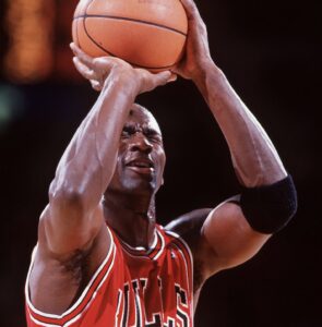 Michael Jordan in a Chicago Bulls jersey taking a free throw with his eyes closed during an NBA game, showcasing his legendary confidence and swagger.