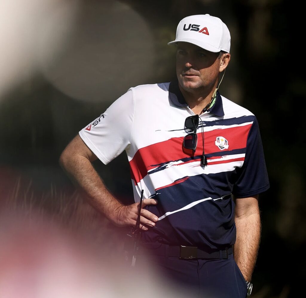 Team USA Ryder Cup captain in white USA cap and red, white, and blue polo shirt standing with hand on hip during 2025 Ryder Cup preparations.
