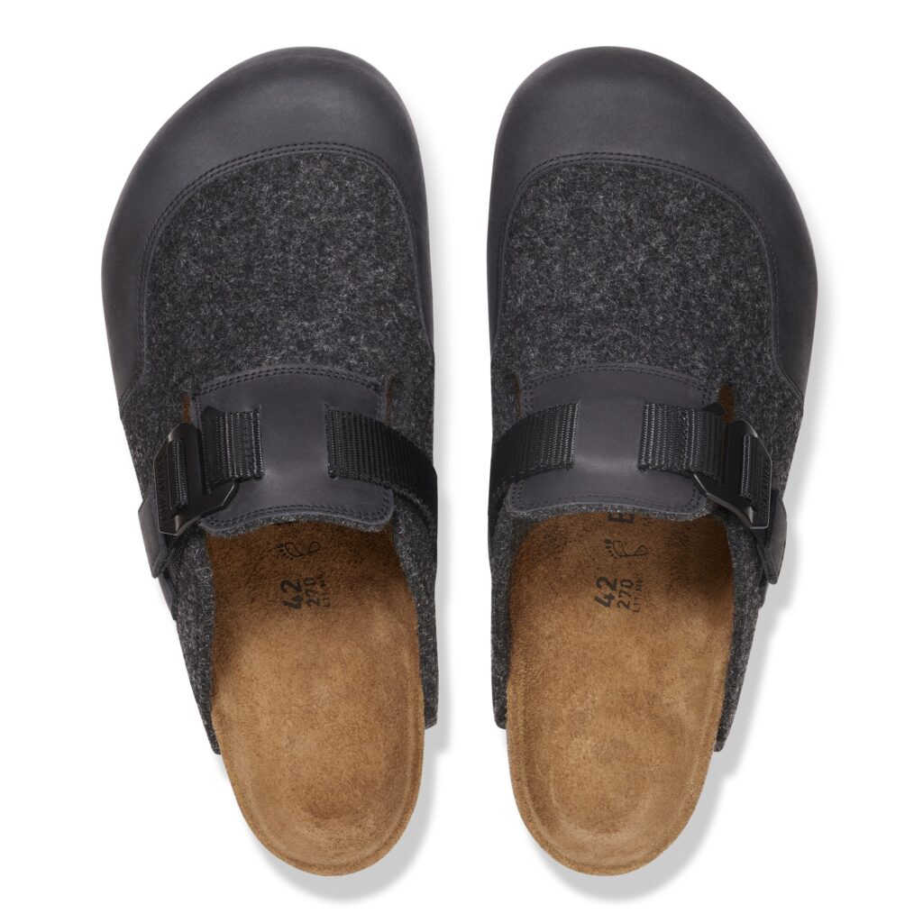 Top-down view of the BIRKENSTOCK Boston clog from the Utility Felt Pack in Anthracite. The shoes feature dark wool felt uppers paired with smooth black leather toe-caps, adjustable black nylon straps with G-hook buckles, and natural cork-latex footbeds—highlighting ergonomic comfort and understated winter styling.