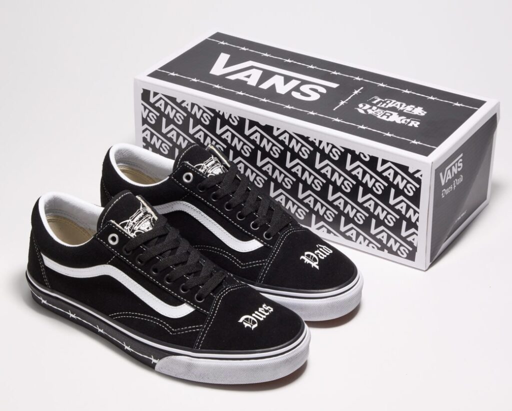Travis Barker x Vans Old Skool “Dues Paid” sneakers displayed beside their co-branded box, featuring black uppers with white side stripes, gothic “Dues” and “Paid” embroidery on the toe boxes, barbed-wire print around the midsoles, and matching monochrome packaging with Vans and Travis Barker logos
