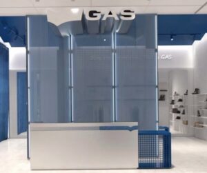 Minimalist GAS Jeans store interior with blue mesh panels, white tiled walls, and modern display shelves showcasing footwear and denim.