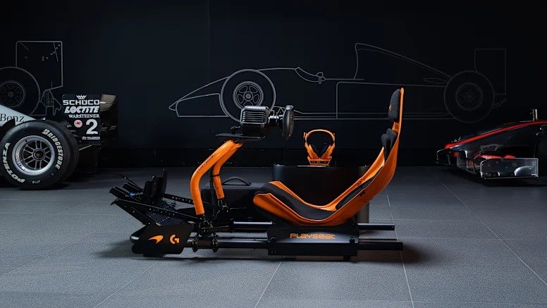 Side profile of the PLAYSEAT® Formula Instinct McLaren Racing Edition simulator, featuring an aerodynamic papaya-orange frame with integrated racing seat, steering wheel mount, and pedal base, set against a dark backdrop with Formula 1 car outlines and racing tires.