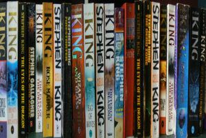 Row of Stephen King books on a library shelf, including titles like The Eyes of the Dragon, Firestarter, Rose Madder, Bag of Bones, Different Seasons, and Christine.