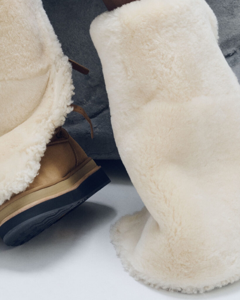 Close-up of the chestnut and cream UGG × sacai thigh-high boots from the Autumn/Winter 2025 collection, featuring soft shearling exteriors and tan suede bases that highlight the collaboration’s blend of warmth and high-fashion design.
