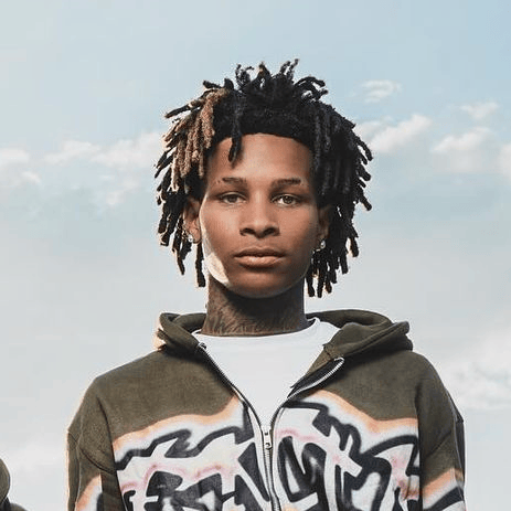 Portrait of rapper Bak Jay wearing a graffiti-patterned zip-up hoodie against a soft blue sky backdrop, embodying the laid-back yet expressive tone of his collaboration with NoCap on “Love on an Island.”