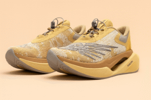 New Balance × Stone Island Tokyo Design Studio FuelCell C_1 sneakers displayed on a soft peach background, highlighting their tan and beige knit upper, sculpted midsole, and magnetic speed-lacing system