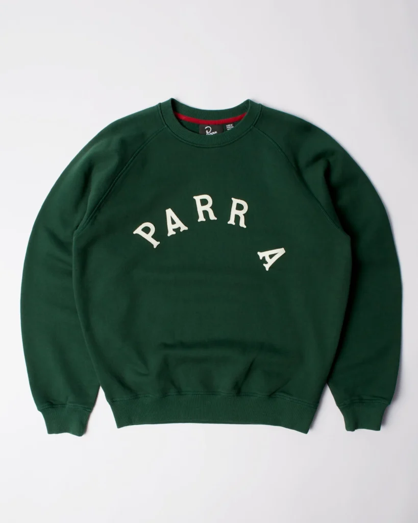 Green by Parra crew neck sweatshirt laid flat on a white background, featuring cream “PARRA” arched appliqué lettering across the chest and visible red neckline detail.