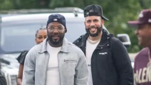 Jeezy and DJ Drama walking outdoors together, Jeezy in a denim jacket and cap, DJ Drama in a black jacket and gold chain, both smiling as they reunite.