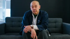 Jeff Staple seated on a grey sofa in a minimalist studio, wearing a navy Arc’teryx jacket and white shirt — reflecting the creative and understated ethos behind the Staple brand and the 21 Series movement.