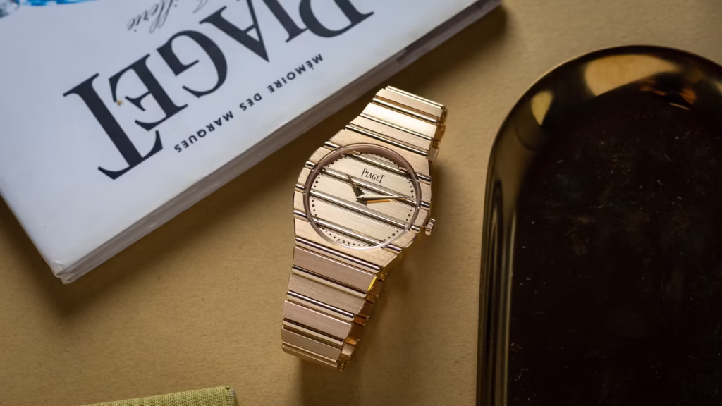 Piaget Polo 79 watch in 18k white gold, displayed on a reflective surface. The integrated bracelet features alternating polished and brushed horizontal gadroons that flow seamlessly into the round case. The minimal gold dial, without numerals, captures the essence of 1980s elegance reinterpreted for modern luxury. The composition emphasizes the watch’s sculptural form and luminous metal texture.