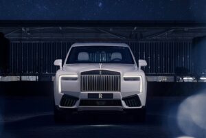 Front view of the Rolls-Royce Cullinan Cosmos, a bespoke SUV finished in Arabescato Pearl, illuminated under moonlight with signature LED headlamps and the Spirit of Ecstasy emblem glowing against a night-sky backdrop.
