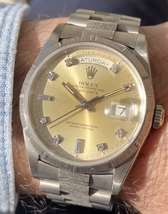 Close-up of a vintage Rolex Oyster Perpetual Day-Date wristwatch with a champagne dial, diamond hour markers, and a brushed white gold case and bracelet, showing the day “Saturday” and date “7” under sunlight.