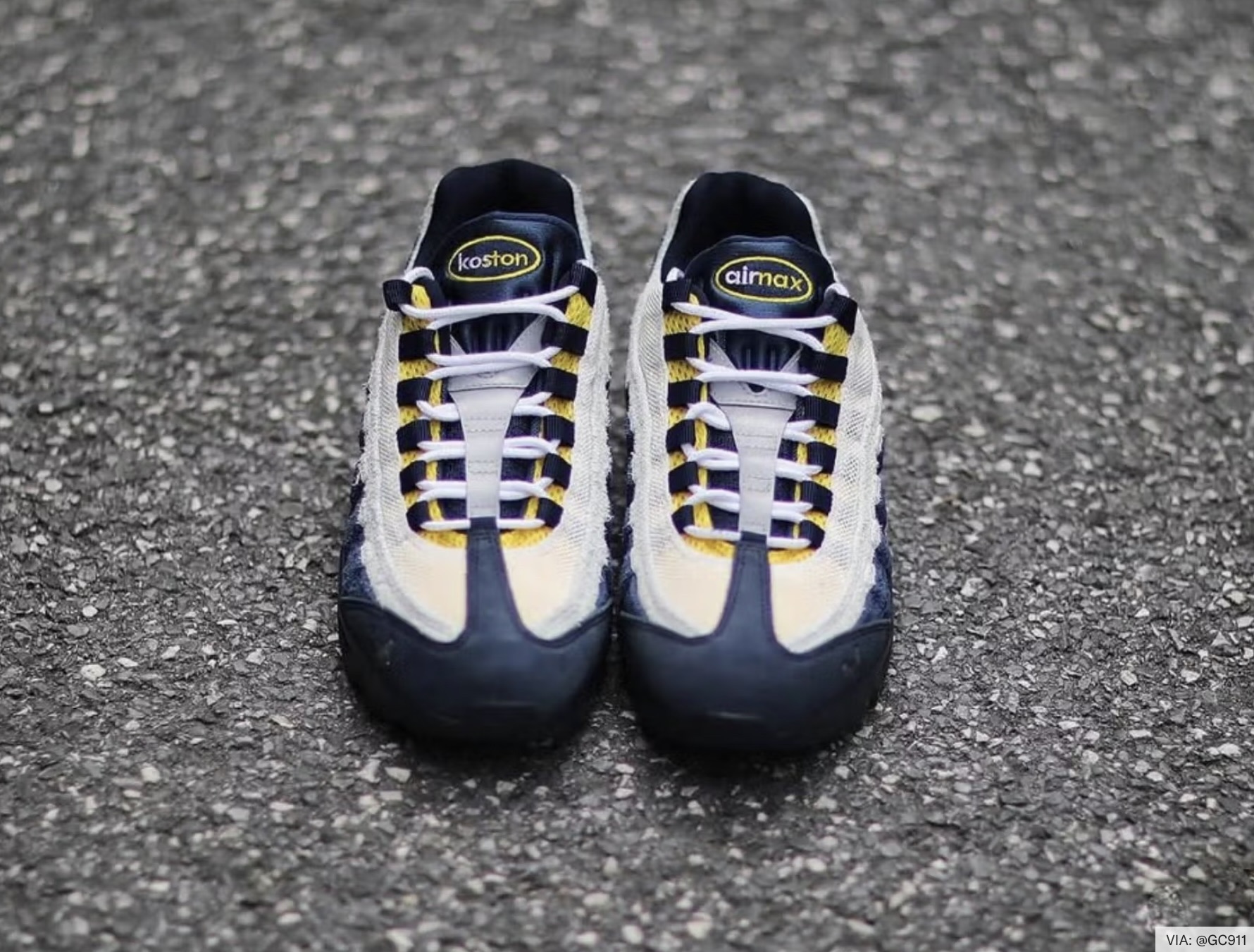 Overhead view of Eric Koston’s Nike SB Air Max 95 sneakers in the “Obsidian / Speed Yellow / Summit White” colorway, photographed on asphalt. The gradient suede panels fade from deep navy to white, with yellow lace loops and co-branded tongue tags reading “koston” and “airmax.”