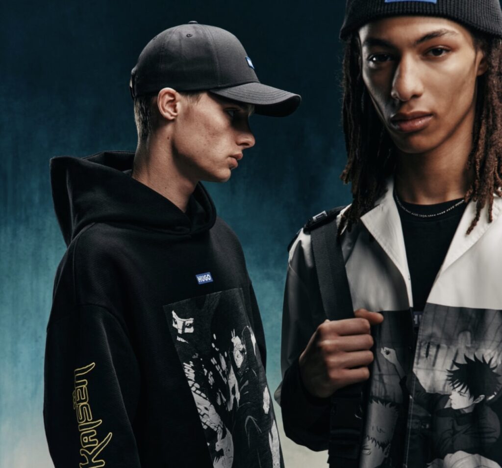 Two male models showcasing pieces from the HUGO × Jujutsu Kaisen capsule collection. The model on the left wears a black hoodie featuring bold anime artwork of the series’ characters, yellow Japanese lettering on the sleeve, and a black HUGO logo cap. The model on the right wears a monochrome zip-up jacket printed with grayscale Jujutsu Kaisen scenes and a black beanie with the HUGO × Jujutsu Kaisen logo, accessorized with a shoulder strap bag, against a dark teal gradient backd