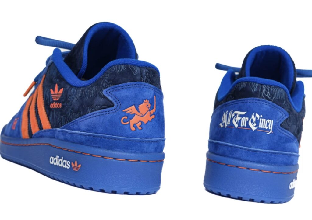 Rear and side view of the adidas Forum Low “All For Cincy” Blue Kit edition, highlighting the orange winged lion FC Cincinnati emblem on one heel, gothic “All For Cincy” lettering embroidered on the other, and orange-stitched adidas branding along the royal-blue suede and navy upper.
