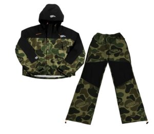 RoughPlay camouflage set featuring a hooded jacket with black paneling and orange drawstring accents, paired with matching camo pants with reinforced black knee sections, displayed on a white background.