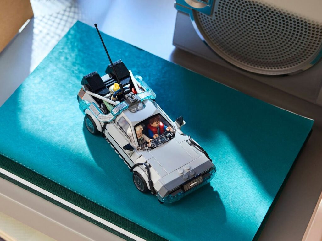 Top view of the LEGO Back to the Future DeLorean Time Machine model placed on a teal surface, featuring Doc Brown and Marty McFly minifigures inside the car with detailed components like the flux capacitor and rear antenna visible.