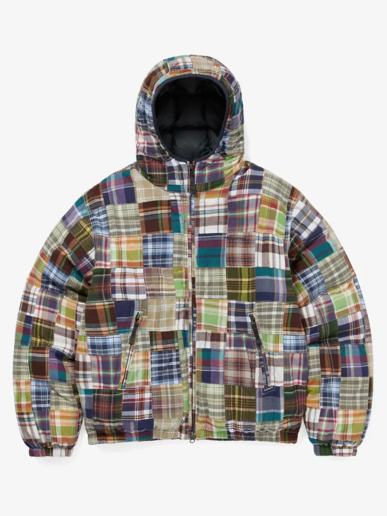 Full front view of the thisisneverthat AW25 Washed Down Puffer Jacket Multi, featuring a hooded silhouette covered in a vibrant patchwork of plaid fabrics in green, blue, brown, red, and beige tones, with two zippered front pockets and elastic cuffs.