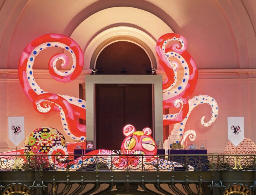 Installation view of Louis Vuitton’s Artycapucines VII presentation at Art Basel Paris 2025, featuring Takashi Murakami’s large pink-and-red polka-dotted tentacle sculptures and colorful flower spheres surrounding the Louis Vuitton display inside the Grand Palais.