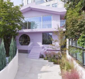 Exterior of Marine Serre’s Hannam House flagship in Seoul, a lavender-colored modernist building designed by Sybarite, featuring a circular window, glass railings, angular rooflines, and landscaped greenery surrounding the minimalist courtyard.