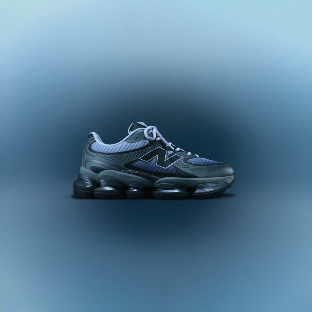 New Balance ABZORB 2000 sneaker in the “Pearl Grey with Black” colourway, featuring a metallic grey and navy mesh upper with black overlays and a sculpted ABZORB midsole, displayed on a smooth blue gradient background.