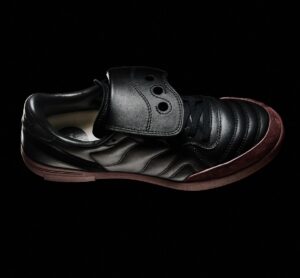 Saucony SILO Fall/Winter 2025 sneaker in black leather with quilted detailing, burgundy suede toe cap, and tonal fold-over lace guard, set against a dark background.