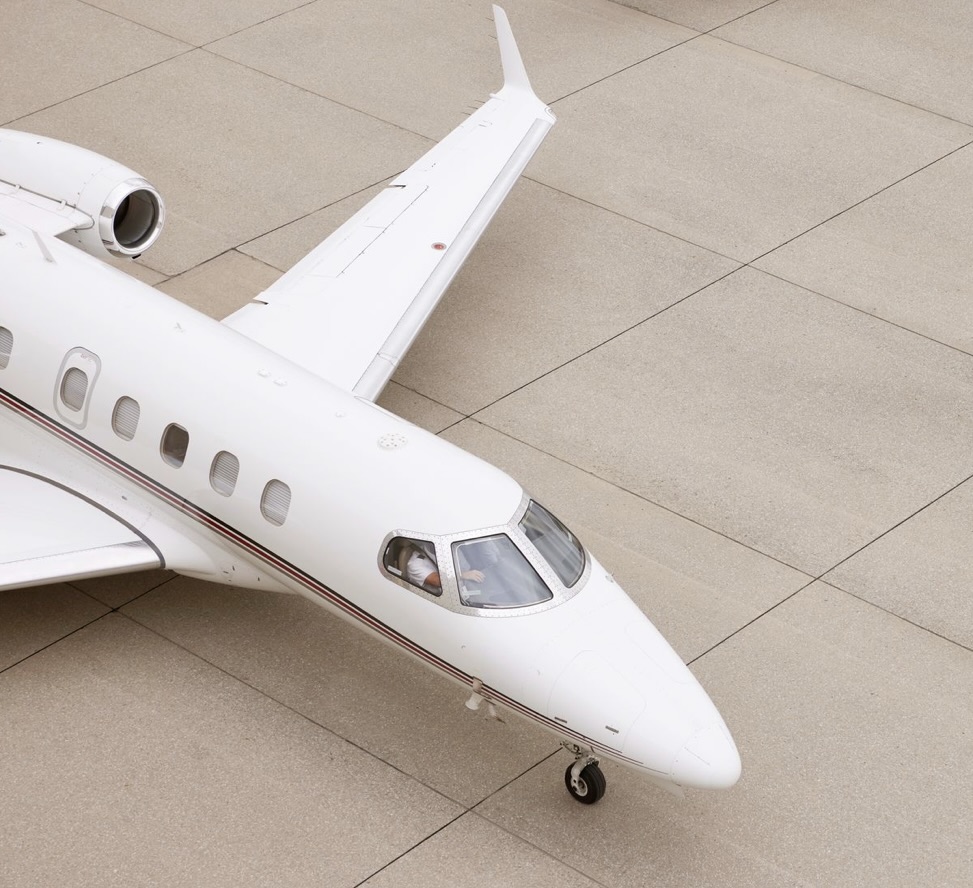 A white NetJets private jet positioned on the tarmac, photographed from above, showcasing the cockpit, wing, and sleek fuselage.