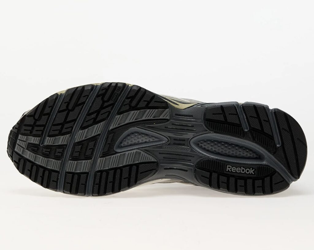 Bottom view of the Reebok Premier Road Ultra Tonal Grey sneaker, showcasing the black rubber outsole with detailed tread pattern, “Transition Bridge” midfoot support, and Reebok logo embossed near the heel for traction and stability design.