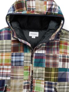 Close-up view of the thisisneverthat AW25 Washed Down Puffer Jacket Multi, showcasing its colorful patchwork of plaid fabrics in greens, blues, browns, and reds, with a black insulated lining and visible brand tag inside the hood.