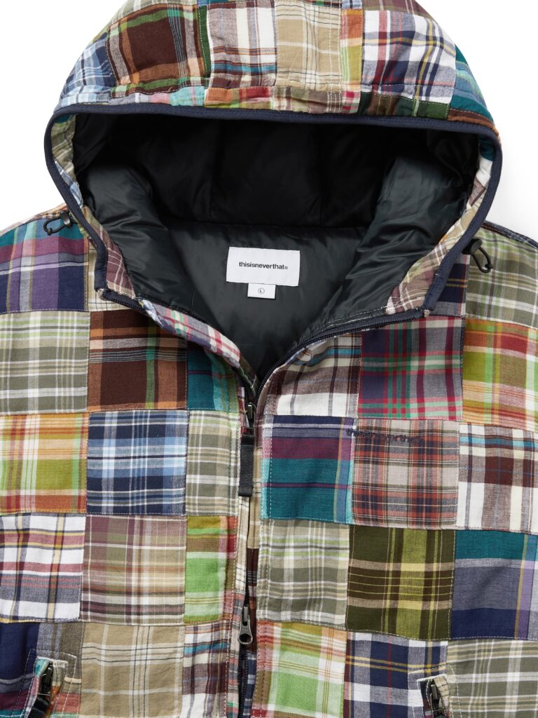 Close-up view of the thisisneverthat AW25 Washed Down Puffer Jacket Multi, showcasing its colorful patchwork of plaid fabrics in greens, blues, browns, and reds, with a black insulated lining and visible brand tag inside the hood.