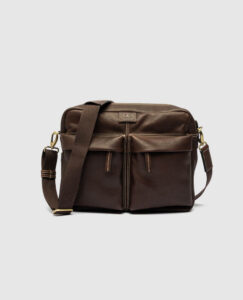 Rodd & Gunn Drury Messenger bag in chocolate brown milled leather, featuring two front zip pockets, contrast stitching, antique brass hardware, and an adjustable fabric-and-leather shoulder strap.
