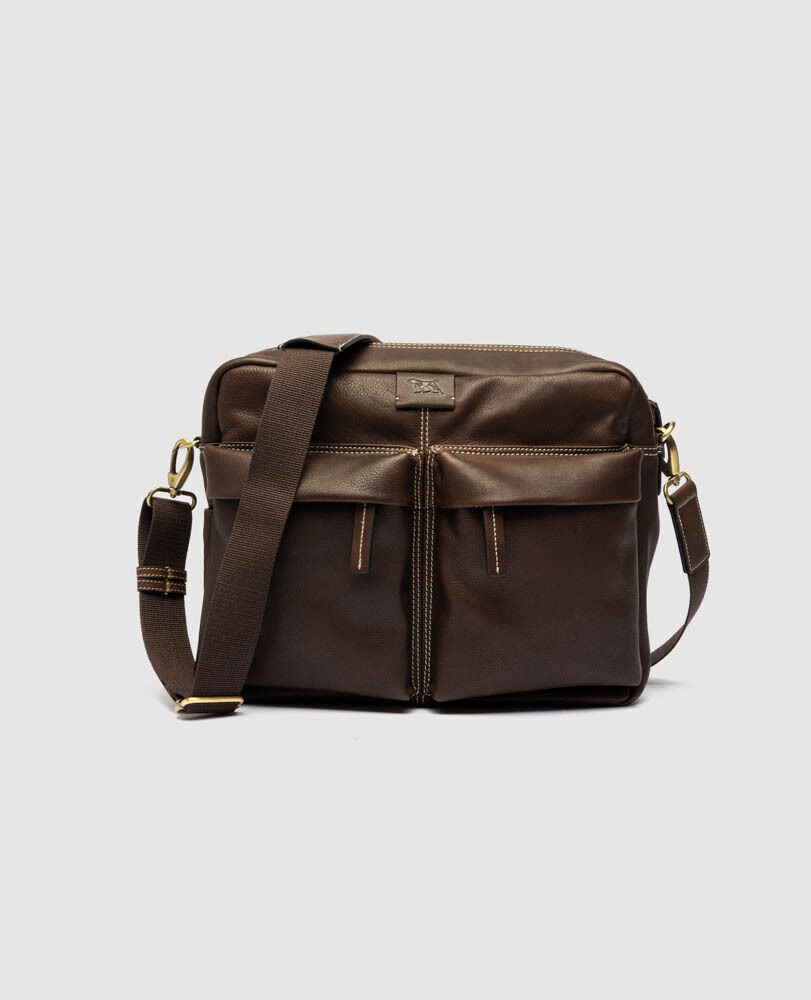 Rodd & Gunn Drury Messenger bag in chocolate brown milled leather, featuring two front zip pockets, contrast stitching, antique brass hardware, and an adjustable fabric-and-leather shoulder strap.