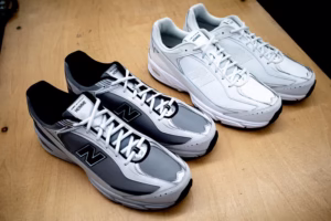 COMME des GARÇONS Homme × New Balance 509 ‘White’ sneaker photographed in close-up, showcasing its minimalist all-white leather construction, perforated upper, tonal ‘N’ logo, and subtle CdG Homme branding. Displayed against a neutral grey studio background highlighting the shoe’s clean lines and sculpted ABZORB midsole.